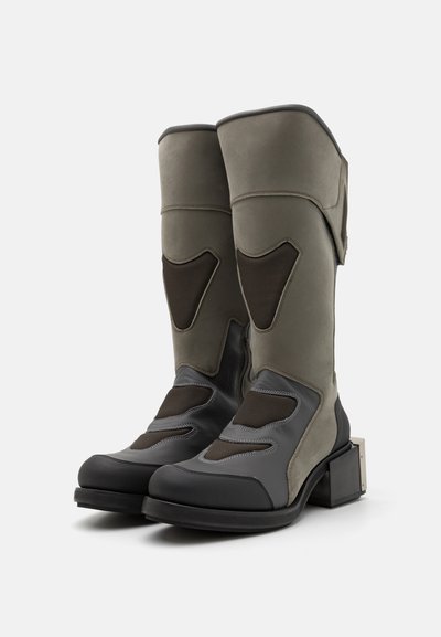 Knee-high saapad, millel on halli ja oliivroheline sile nahk, võrgusilmast detailid ja tükiline pöial, millel on metallist aksent.