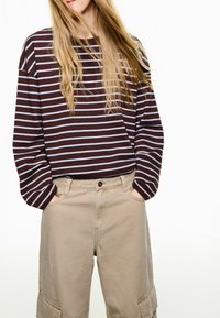 Hnědý a světle modrý svetr s pruhy a volnými rukávy, doplněný béžovými širokými kalhotami s bočními kapsami a viditelným šitím.