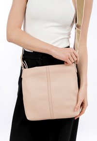 Borsa a spalla in pelle rosa con una texture liscia, caratterizzata da due cuciture verticali e una tracolla beige. Chiusura con cerniera visibile sul lato.