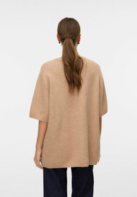 Beige übergroßer Strickpullover mit kurzen Ärmeln, gerippten Bündchen und einer lockeren Passform. Weicher Stoff, Rückansicht, kombiniert mit dunklen Jeans.