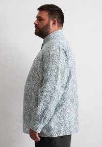 Himmelblaues Hemd mit Knöpfen, das ein florales Muster in dunkleren Farbtönen aufweist. Hergestellt aus Baumwolle, hat es eine lockere Passform und lange Ärmel.