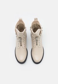 Beige leather ankle boots with a rounded toe, side zippers, and decorative metal studs along the front and sides. Black rubber sole.
