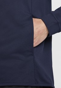 Camiseta atlética azul marino con un tejido texturizado y transpirable, con un bolsillo lateral y un diseño de puños ajustados.