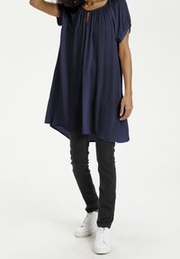 Tunique bleu marine à manches courtes, encolure avec ouverture en œillet, coupe décontractée, associée à un jean skinny noir et des baskets blanches.