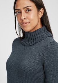 Tmavě modrý pletený svetr s vysokým ribbed límcem, s texturovaným povrchem a přiléhavými rukávy, vyrobený z měkkého, elastického materiálu.