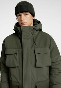 Olivgrön isolerad jacka med hög krage, justerbar dragskohuva och flera framfickor. Strukturerad stickad mössa.