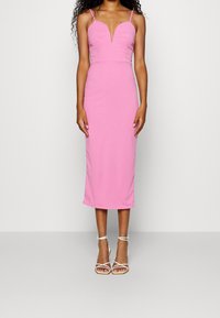 Bloemige roze midi-jurk met een aansluitend lijfje, V-hals en dunne bandjes. Gladde stof met een lichte glans, gedragen met witte sandaaltjes met bandjes.