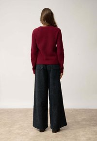 Bordeaux gebreide trui met een gestructureerde afwerking, gecombineerd met wijde zwarte corduroy broek. De outfit heeft een getailleerd bovenstuk en een losse onderzijde.