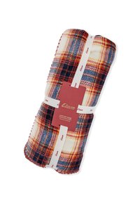 Pluszowy koc w kratę w ciepłych kolorach czerwieni, pomarańczy i niebieskiego. Z białym przeszyciem oraz czerwoną metką z nazwą marki i instrukcjami pielęgnacji.