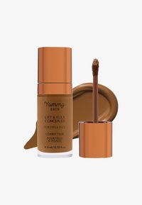 Correttore marrone in un flacone trasparente con un cappuccio metallico rosa oro. Include un applicatore affusolato. Campionatura di prodotto cremoso sul lato.