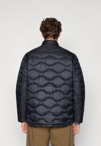 Puffjacka i mörk marinblå med en kviltad design som har överlappande ovala mönster. Slät, glansig tyg och ståkrage.