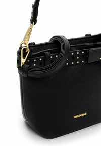 Czarna skórzana torebka o teksturowanej powierzchni, ze złotymi akcentami i odpinanym paskiem. Na górnej krawędzi znajduje się ozdobny pasek z kropkami.