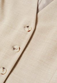 Tissu beige avec trois boutons translucides cousus présentant des tourbillons marron foncé, faisant partie d'un vêtement avec un col plié.