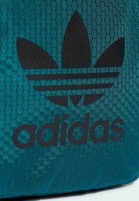 Borsa a rete turchese con logo Adidas nero, motivo esagonale distintivo e texture liscia, progettata per una leggerezza durevole.