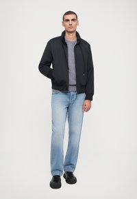 Sort bomberjakke med lynlås foran, elastiske manchetter og snoretræk, båret over en grå sweatshirt med rund hals, parret med lyseblå jeans og sorte sko.