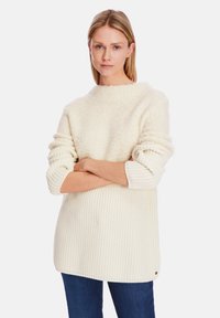 Chunky white sweater with a soft, textured finish, ribbed sleeves, and a loose fit. Notable logo accent near the hem.