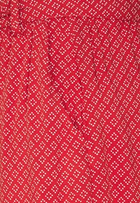 Tissu rouge avec un motif de diamants blancs et de petits points. Design plissé avec une ceinture. Texture douce, matériau léger.
