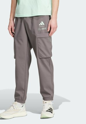 Pantalon cargo gris à jambes droites avec poignets élastiques et logos sur la cuisse portée avec des baskets et une chemise vert clair.