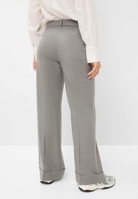 Grijze, wijde broek met een subtiel houndstoothpatroon, voorzien van een op maat gemaakte tailleband en achterzakken. Gemaakt in combinatie met wit- en zwartkleurige sneakers.