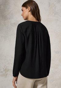 Svart långärmad blus med en strukturerad, skrynklig design, med rund halsringning och veckdetalj längs baksidan.