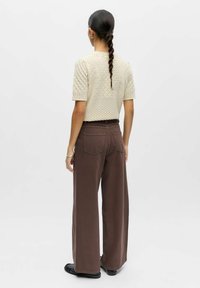 Haut beige en maille avec manches courtes, associé à un pantalon large marron avec poches arrière. Texture lisse et coupe décontractée.