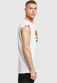 Hvid bomulds ærmeløs T-shirt med et flerfarvet grafisk print af en solnedgang med palmer og teksten "Love". Blød tekstur, afslappet pasform.