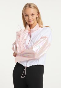 Hvid zip-up jakke med iriserende rosa ærmer og elastisk kant, der har en snor i taljen og en cirkulær lynlåstrækkerr.