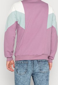 Módní mikina s levandulovým tělem, bílými a světle modrými ramenními panely, ribovanými manžetami a lemem, spárovaná se světlými modrými džíny.