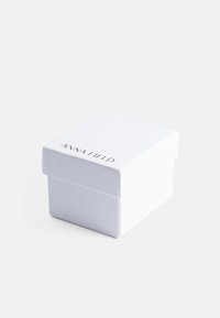 Bela pravokotna škatla z dvignjenim pokrovom, na sprednji strani je črn napis "ANNA FIELD", gladka tekstura, minimalsistična zasnova.