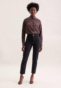 Brown patterned button-up shirt paired with high-waisted black jeans and strappy heels. Smooth fabric with a sleek fit and button detailing.