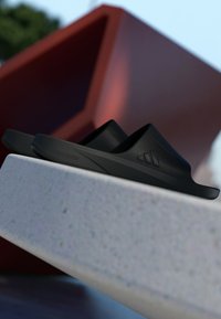 Black slide sandals made of smooth rubber with a contoured footbed. Features a subtle logo and a minimalistic design.