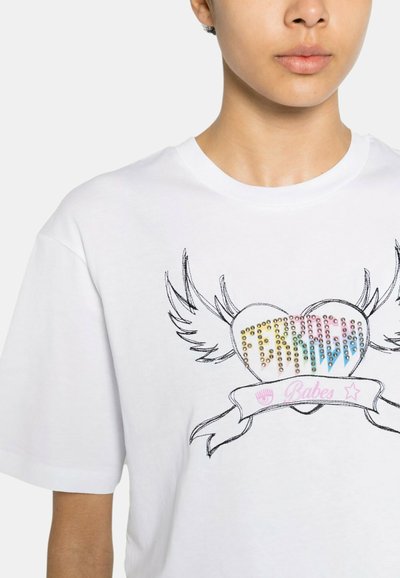 Maglietta bianca in cotone con un design di cuore colorato in strass con ali, un nastro rosa sottostante e la parola "Babes" scritta in corsivo.