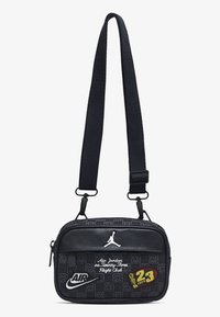Čierna crossbody taška s textúrovaným povrchom, s bielym logom Jordan, označením Nike a vyšívanými nášivkami. Obsahuje nastaviteľný popruh.