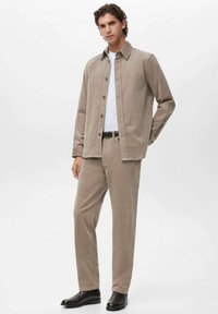 Jachetă de catifea bej cu pantaloni asortați, închidere cu nasturi, croială slim, mâneci lungi și o textură netedă. Purtați cu un tricou alb și o centură neagră.