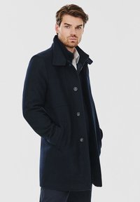 Granatowy wełniany płaszcz z kołnierzem, z przodem zapinanym na guziki i kieszeniami po bokach. Gładka tekstura z dopasowanym krojem i minimalnymi detalami.