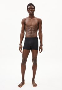 Schwarze Boxershorts aus weichem, elastischem Stoff, mit einem enganliegenden Design und einem glatten Bund. Das Modell steht barfuß vor einem schlichten Hintergrund.
