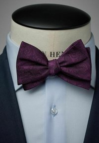 Lila paisley-fluga gjord av texturerad tyg, säkrad med en mittknut, bärs över en ljusblå skjorta och en mörk kavaj.