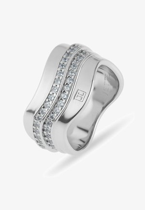 Large bague argentée à la forme incurvée, ornée de deux rangées de petites pierres claires et d'un logo gravé sur l'anneau.