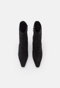 Botines de ante negro con punta afilada, presentan una cremallera en el lateral y una textura suave. Diseño clásico con una silueta elegante.