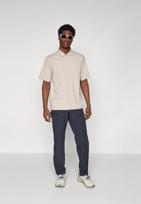 Helebeeži lühikeste varrukatega särk krae ja taskuga koos tumesiniste pükstega. Täiendatud valgete ja hallide tossude ning päikeseprillidega.