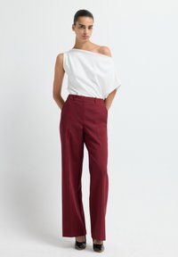 Haut blanc à une épaule en tissu drapé, associé à un pantalon cintré taille haute bordeaux. Des escarpins noirs à bout pointu viennent compléter l'ensemble.