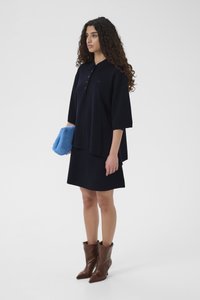 Tricou polo supradimensionat, de culoare bleumarin, cu mâneci scurte și guler, asortat cu o fustă în aceeași nuanță. Cizme maro, cu vârf ascuțit, până la gleznă și o geantă plic albastru deschis.