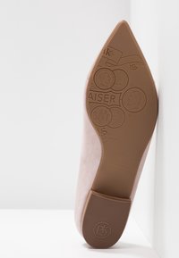 Chaussure en daim rose clair avec un bout pointu et une semelle en caoutchouc marron. La semelle est ornée de motifs en relief et du nom de la marque, "Peter Kaiser".