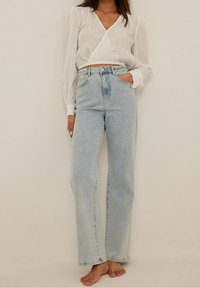 Hellblaue hochwaist Jeans mit geraden Beinen, aus Denim gefertigt. Kombiniert mit einem weißen Langarmtop im Wickelstil, das puffärmel hat.