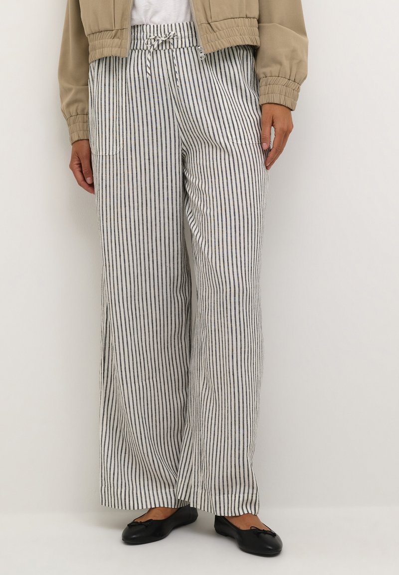 Striped wide-leg pants in light fabric, featuring vertical navy and white stripes, elastic waistband, and side pockets. Black flats are worn.