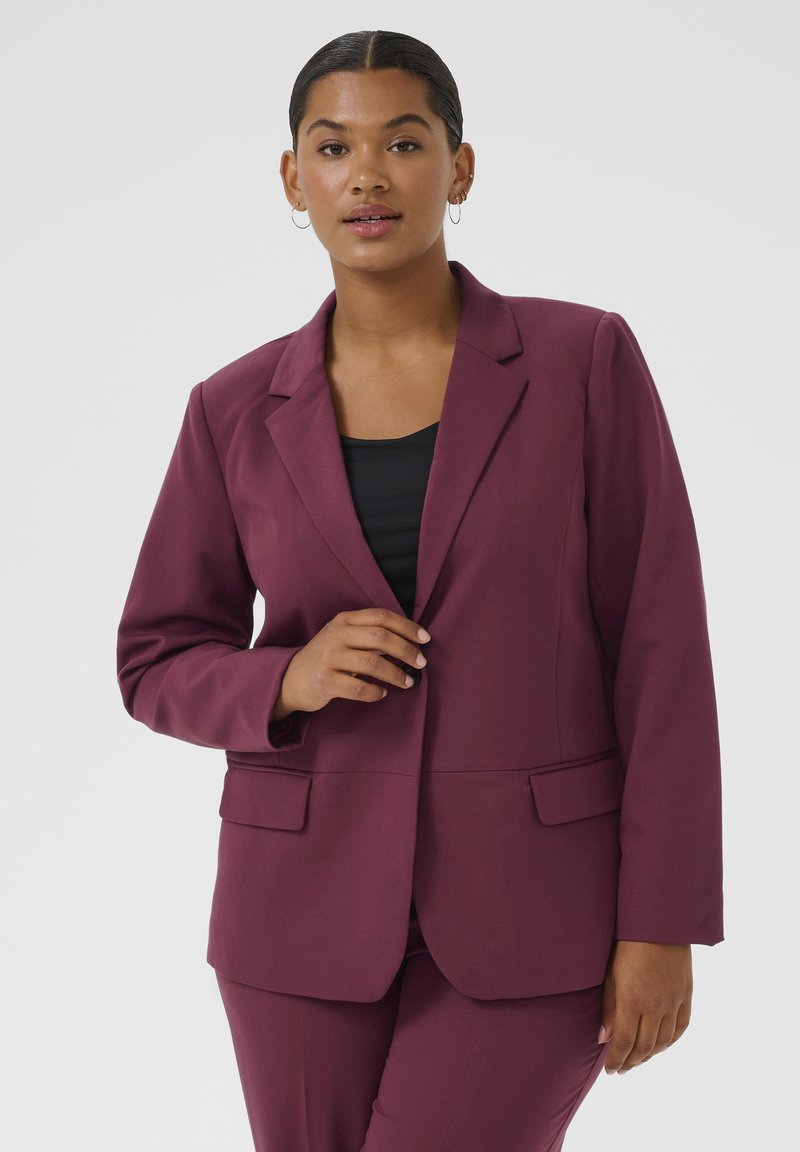 Bordeauxfarbener Blazer mit Reverskragen, zwei vorderen Taschen, taillierter Passform und glattem Stoff, kombiniert mit einem schwarzen Oberteil darunter.