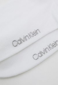 Balti kojinės su raižyta tekstūra ir sidabriniu logotipu, ant kiekvienos kojinės esantis užrašas "Calvin Klein". Minkštas audinio medžiaga.