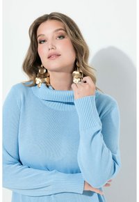 Jasnoniebieski sweter z żebrowanym golfem i mankietami, z teksturowanym splotem. Modelka nosi duże, złote kolczyki.