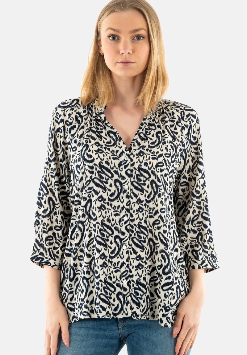 Blusa a motivi con sfondo crema e design astratti blu navy; maniche lunghe, chiusura a bottoni frontale e vestibilità rilassata.