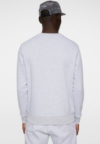 Grå bomullströja med ribbade mudd och nederkant, med en enkel textur. Baksidan har en enkel design utan logotyper eller mönster.